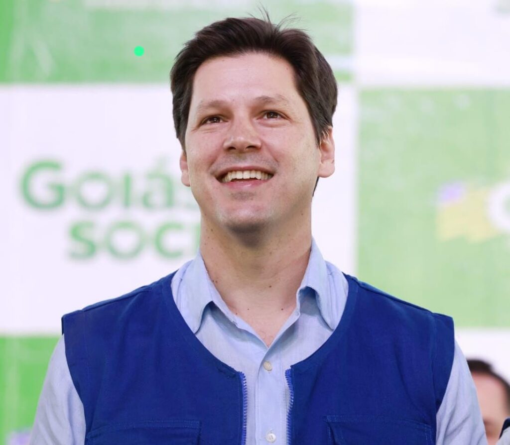 Foto Daniel Vilela sorrindo. usa uma camisa azul clara com colete azul por cima.