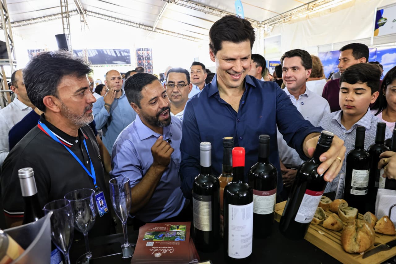 Daniel Vilela durante a abertura da Feira #NoEntornoTem, em Brasília, rodeado de pessoas, lendo o rótulo de um vinho, um dos produtos da feira.